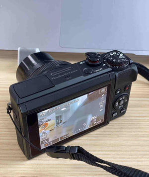 Side view of the black Canon PowerShot G7 X Mark III camera with its zoom lens fully extended on a wooden desk.
