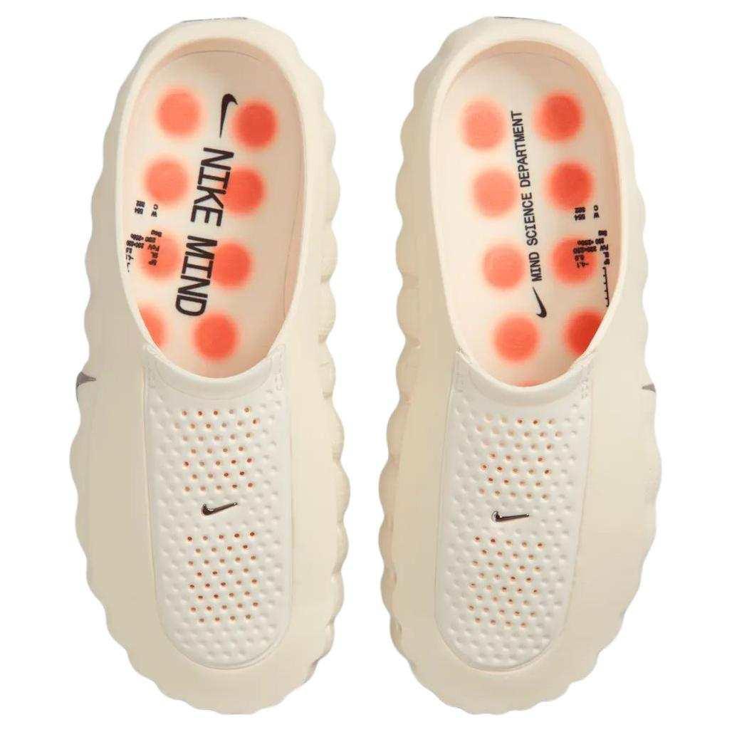 Top-down view of the Nike Mind 001 shoes in off-white, showing the branded footbed inserts and vibrant apricot orange massage pods inside.