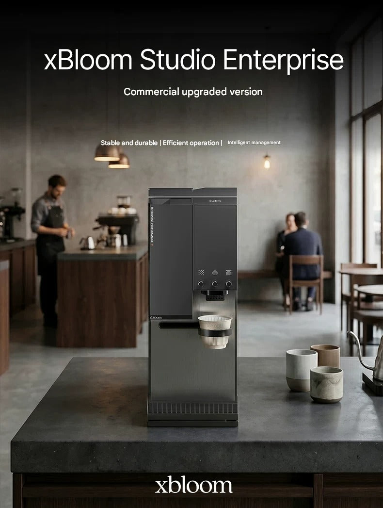 Matte black xBloom Studio Enterprise commercial automatic coffee machine placed on a dark countertop inside a modern specialty coffee shop.